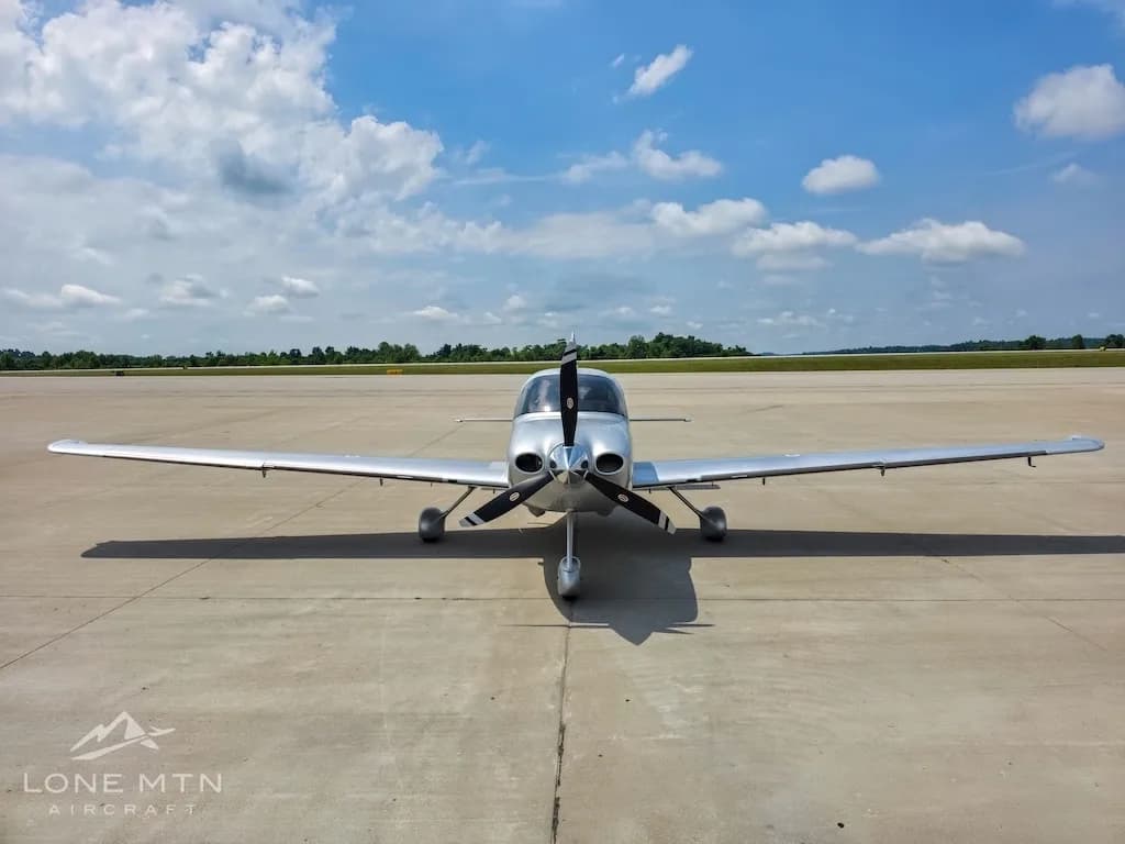 A silver Cirrus SR22 aircraft (N68007) viewed head-on, parked on an airfield under a partly cloudy sky.
