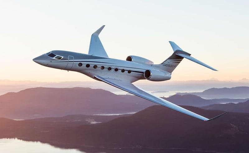 A Gulfstream G650ER flying over a mountainous landscape.