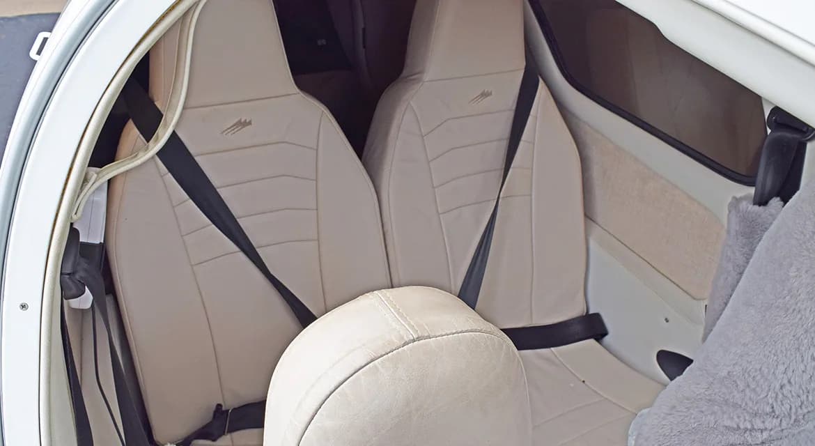 The light-colored leather interior seats of a small aircraft cabin with black seatbelts.