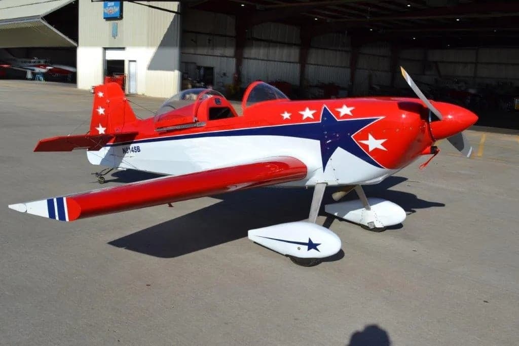 A red and white aircraft with stars on the tail and wings is parked in front of a hangar.