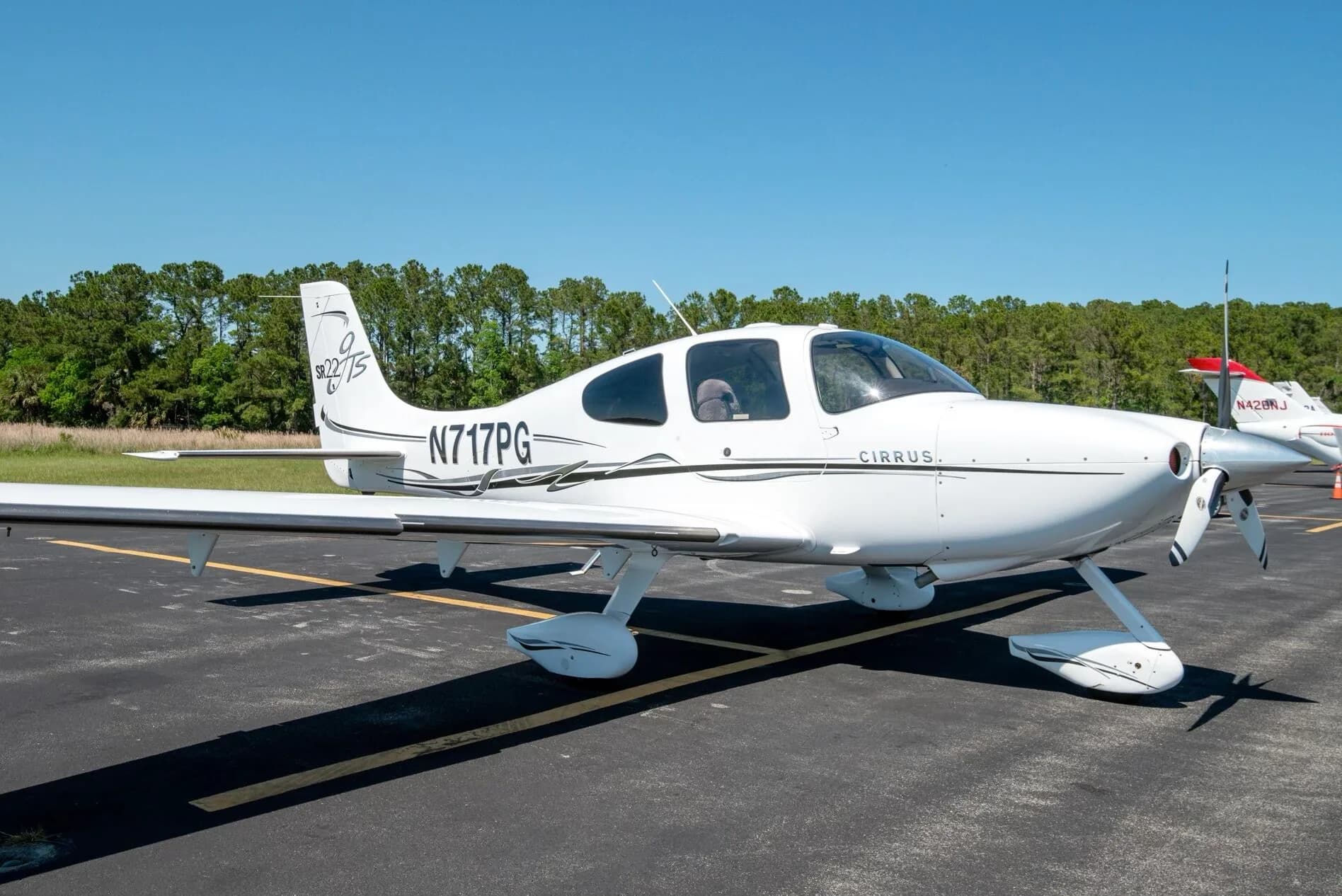 Side view of a white Cirrus SR22T aircraft N717PG with black and grey stripes parked on an airfield.