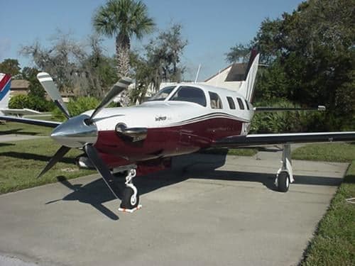 A Piper JetPROP aircraft is parked on the tarmac with a white and maroon paint scheme.