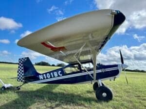 A blue and white ACA aircraft, registration N101BC, parked on a grassy field under a blue sky.