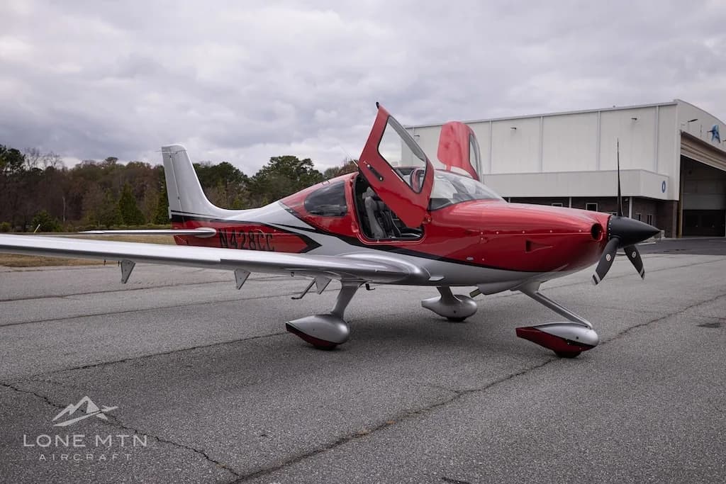 A front-side view of the red and silver Cirrus Vision Jet (N428CC) with its gull-wing doors open, parked on an asphalt tarmac.