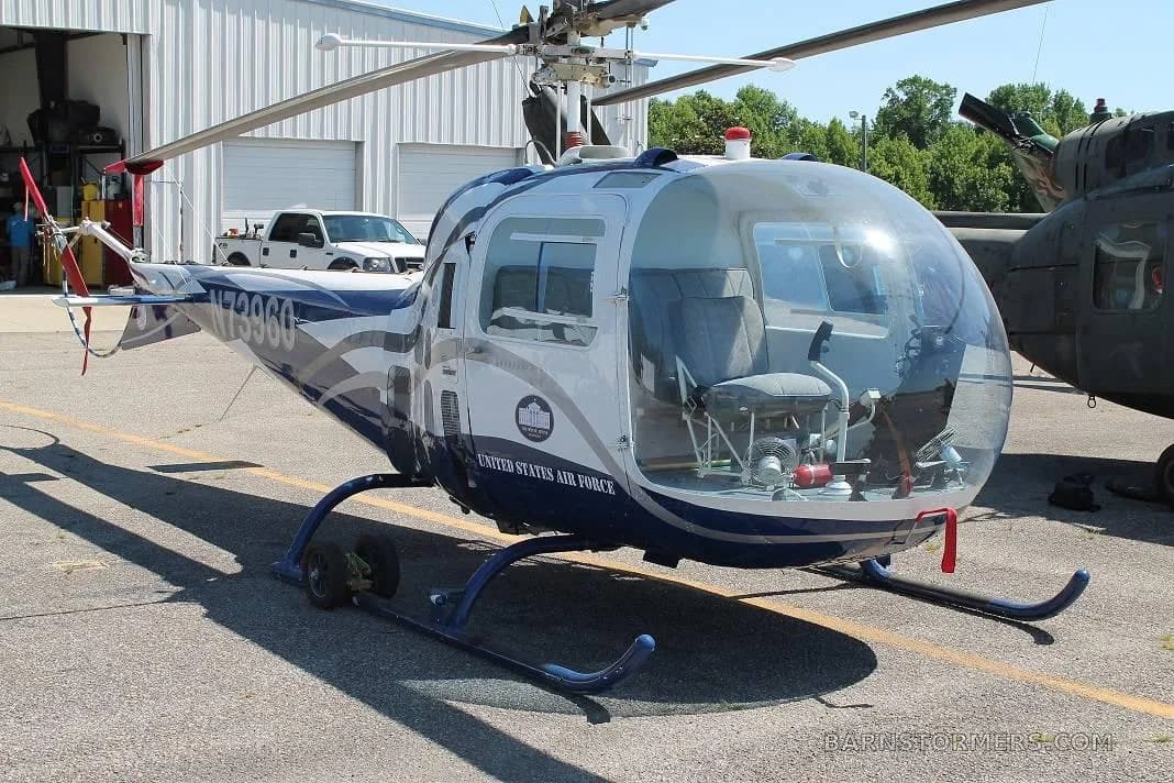 A white and blue helicopter with 'UNITED STATES AIR FORCE' text and registration N73960, parked on asphalt with a white truck and hangar in the background.