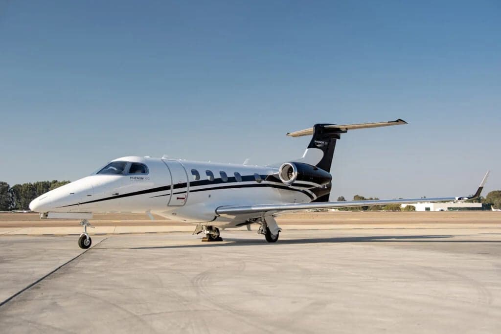 A Phenom 300 aircraft with a white and black paint scheme is parked on the tarmac.