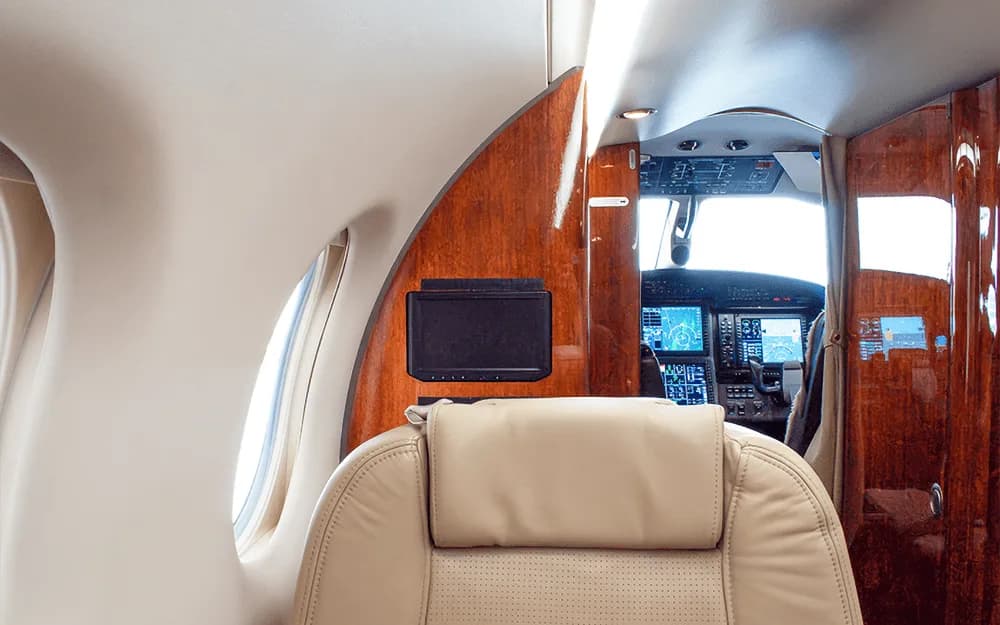 View from the aircraft cabin into the cockpit, showing the instrument panel and beige passenger seats.