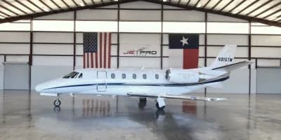 A Citation CJ3+ is parked in a hangar with American and Texas flags in the background.