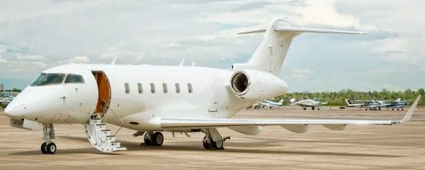 A white Bombardier Challenger aircraft is parked on the tarmac with the door open.
