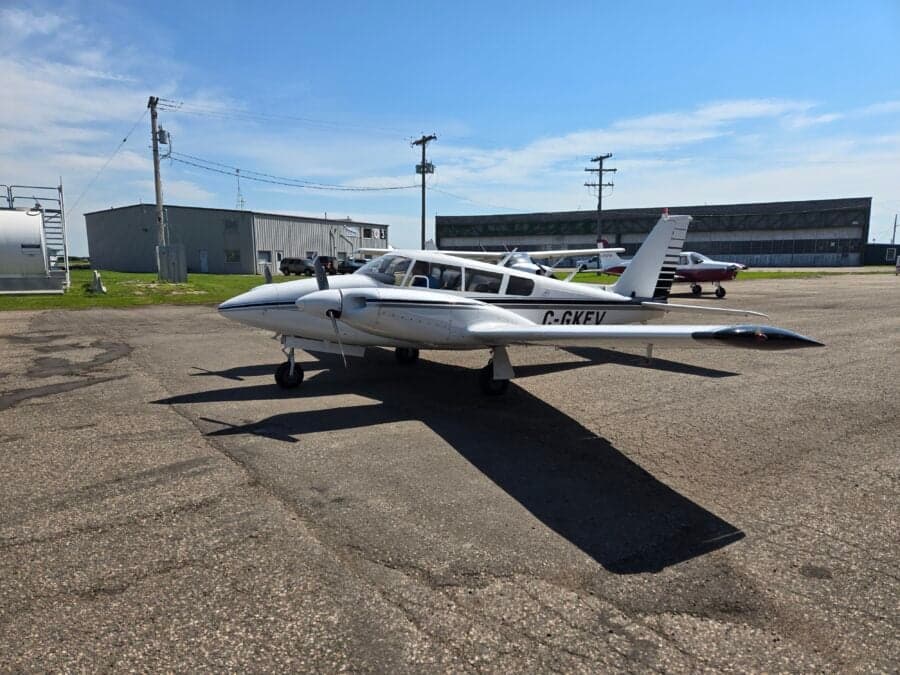 A white and black Piper PA-39 Twin Comanche is parked on the tarmac.