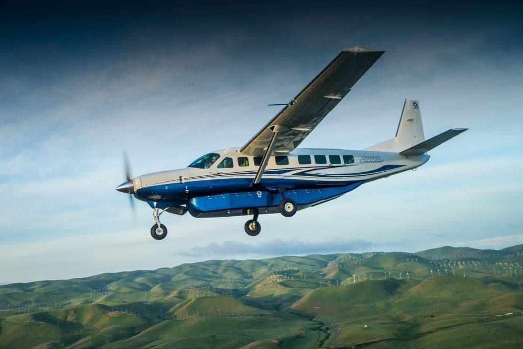 A Cessna Grand Caravan in flight over a hilly landscape.
