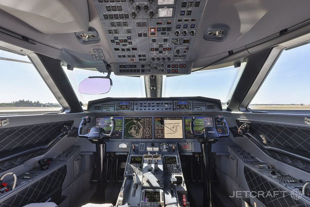 The modern glass cockpit of a Gulfstream business jet with multiple display screens and control panels.