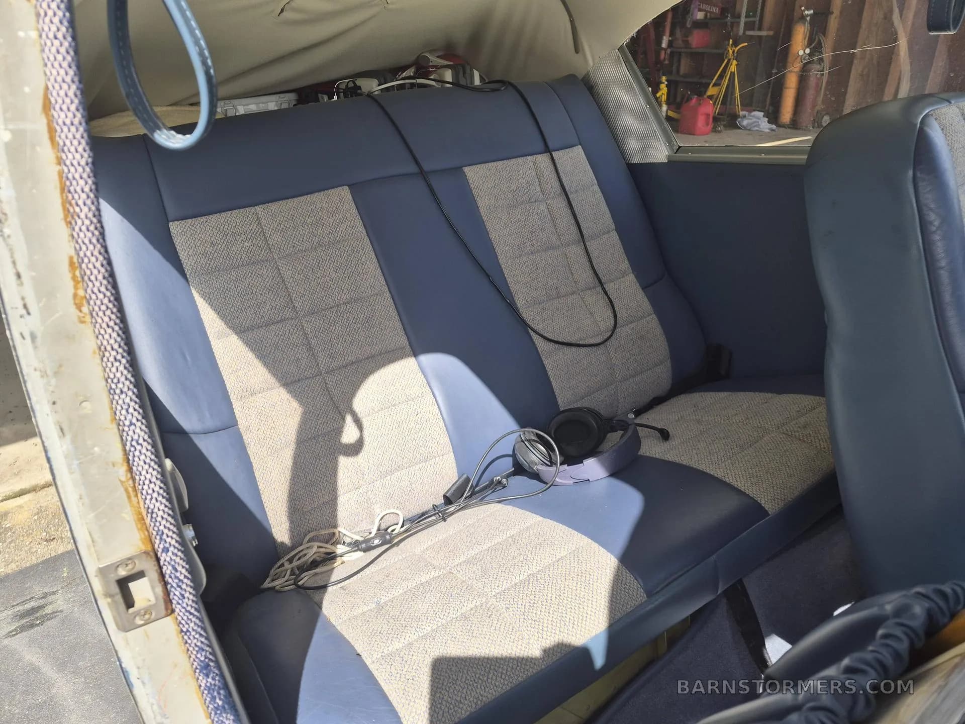 The rear cabin seats of a small aircraft, upholstered in blue and patterned fabric, with a headset on the seat.