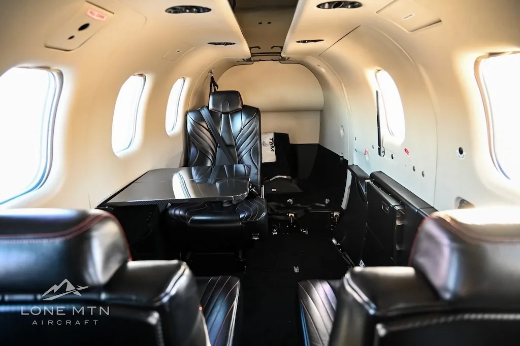 The luxurious black leather interior cabin of a TBM 940 aircraft, featuring a table and passenger seating.