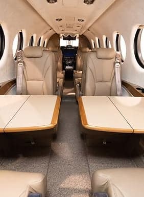 Interior view of an aircraft cabin with leather seats and wooden tables.