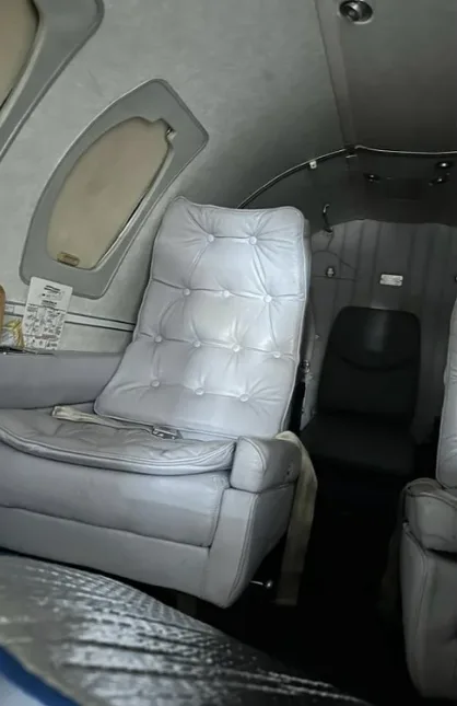 The aircraft's interior cabin with light gray tufted leather seats and small oval windows.