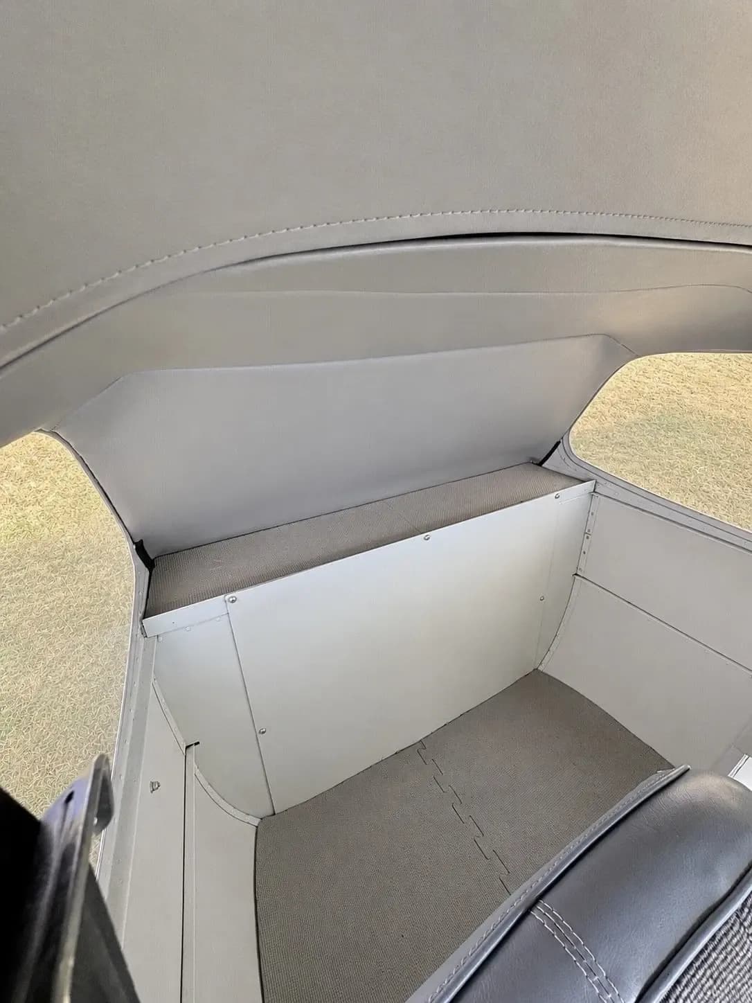 The rear cargo or storage area of a small aircraft cabin, with light grey paneling and flooring.