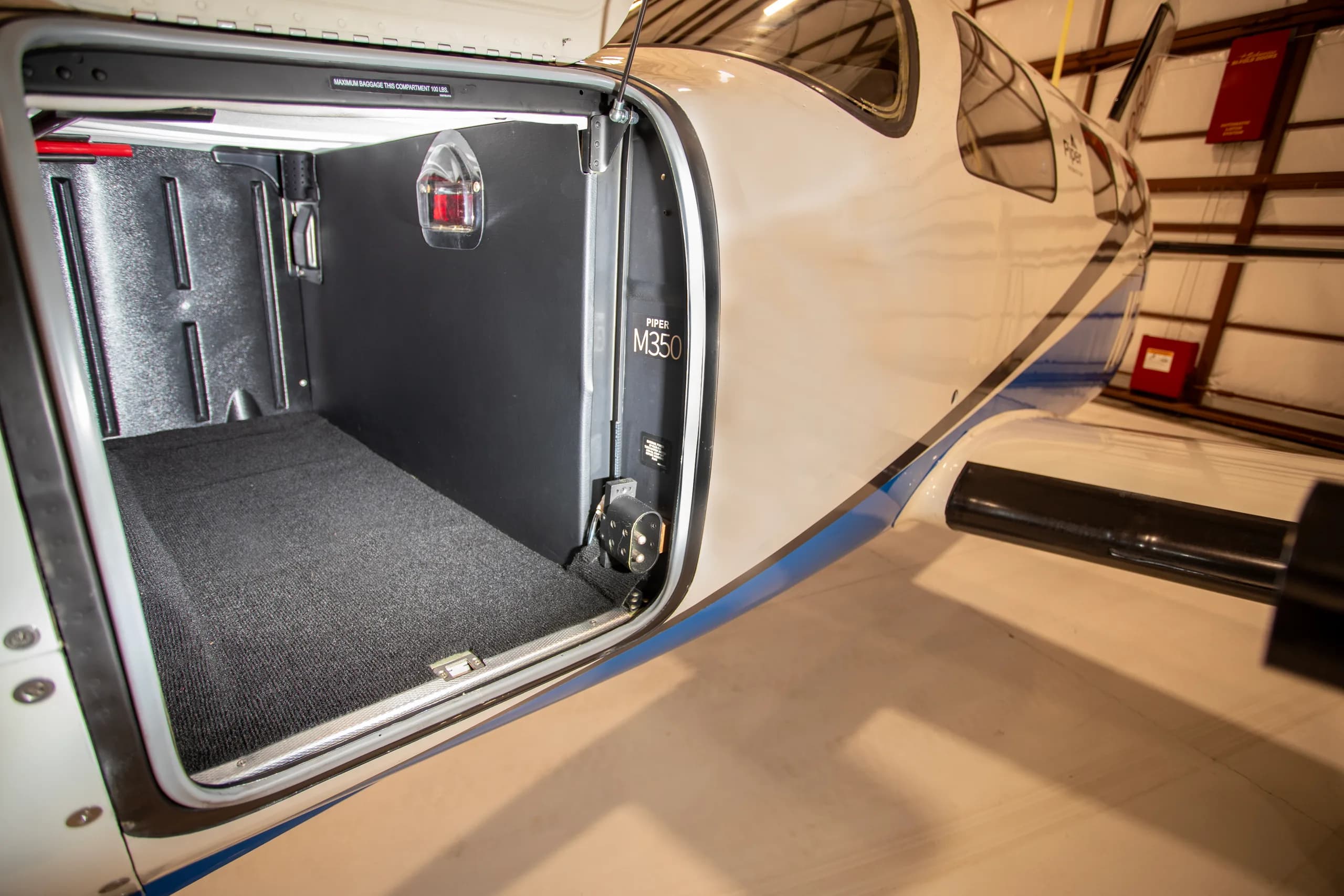 The open cargo compartment of a Piper M350 aircraft, showing the carpeted floor and black interior.