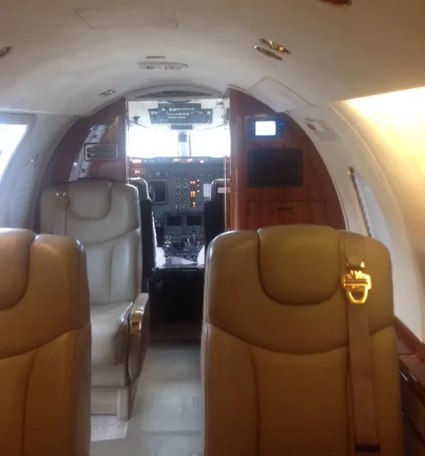 An interior view of an aircraft cabin with beige seats, looking towards the cockpit area.