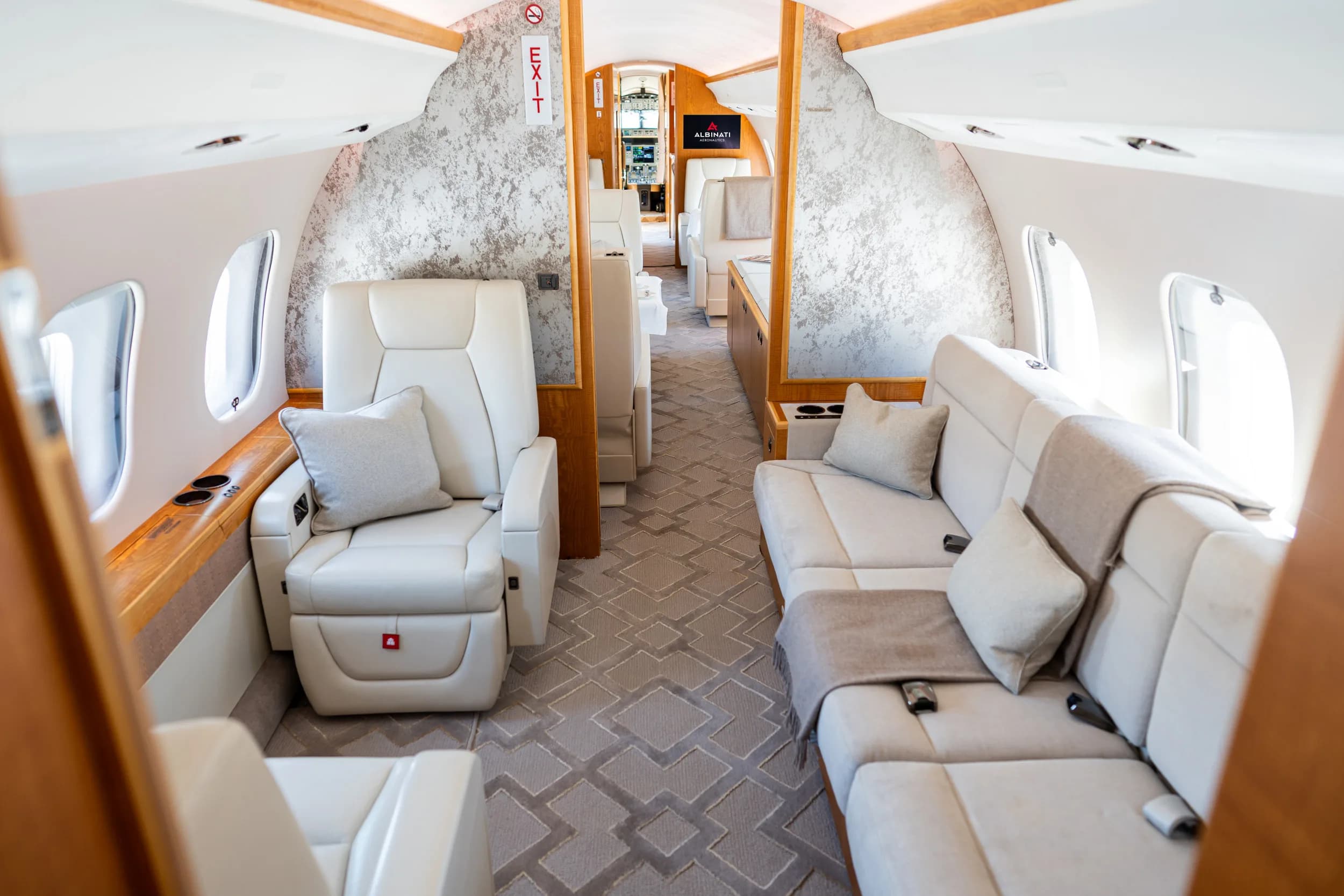 A spacious private jet cabin interior with cream leather seats, a sofa, and patterned carpet.