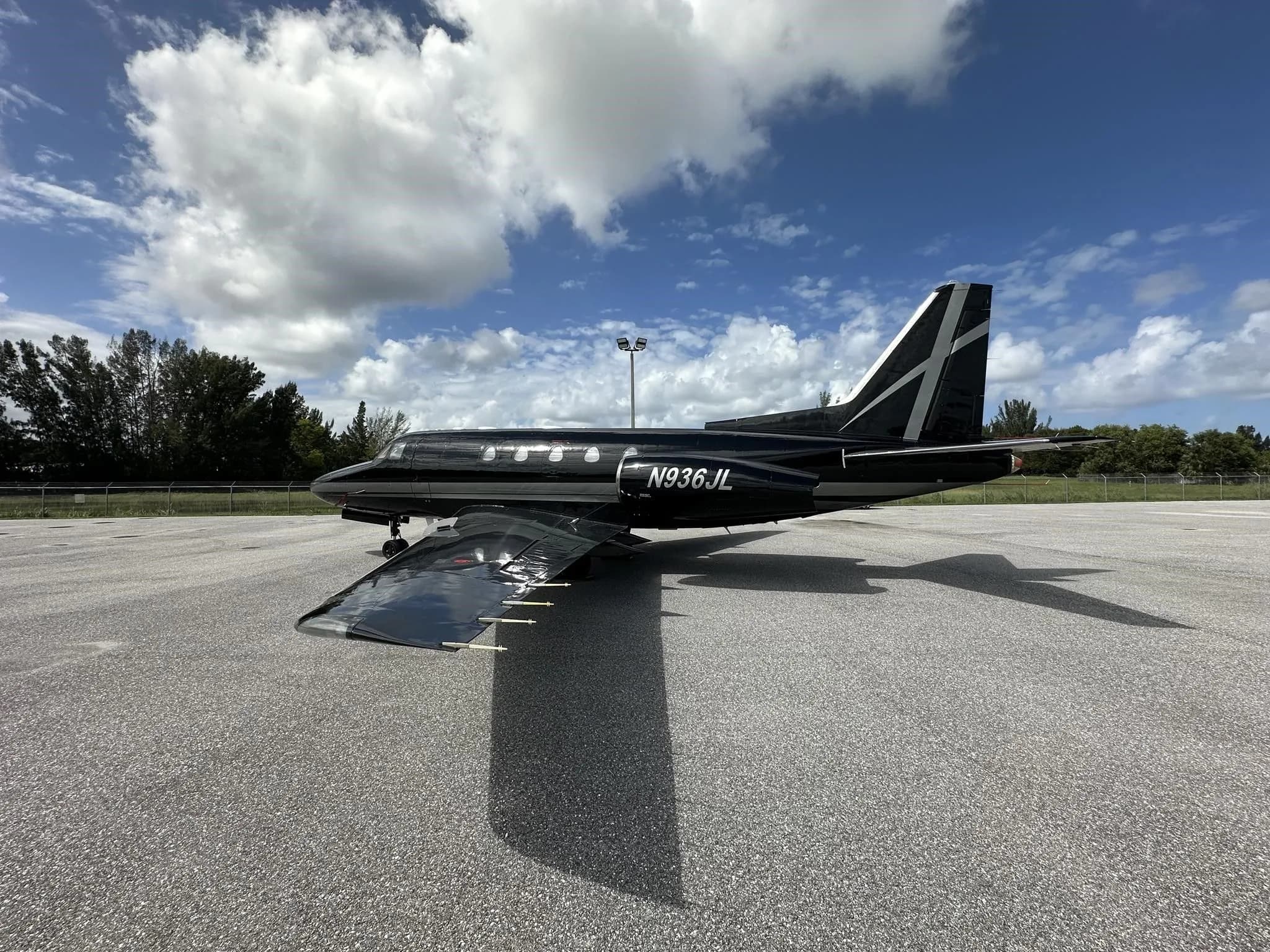 A black and silver business jet, N936JL, viewed from the rear-side, showing its full wing span and tail.