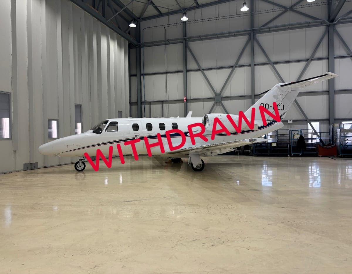 A side view of the OO-CCJ aircraft in a hangar, with a white paint scheme and red stripes.
