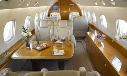 A luxurious aircraft cabin interior with cream leather seats, a polished wooden table, and refreshments.