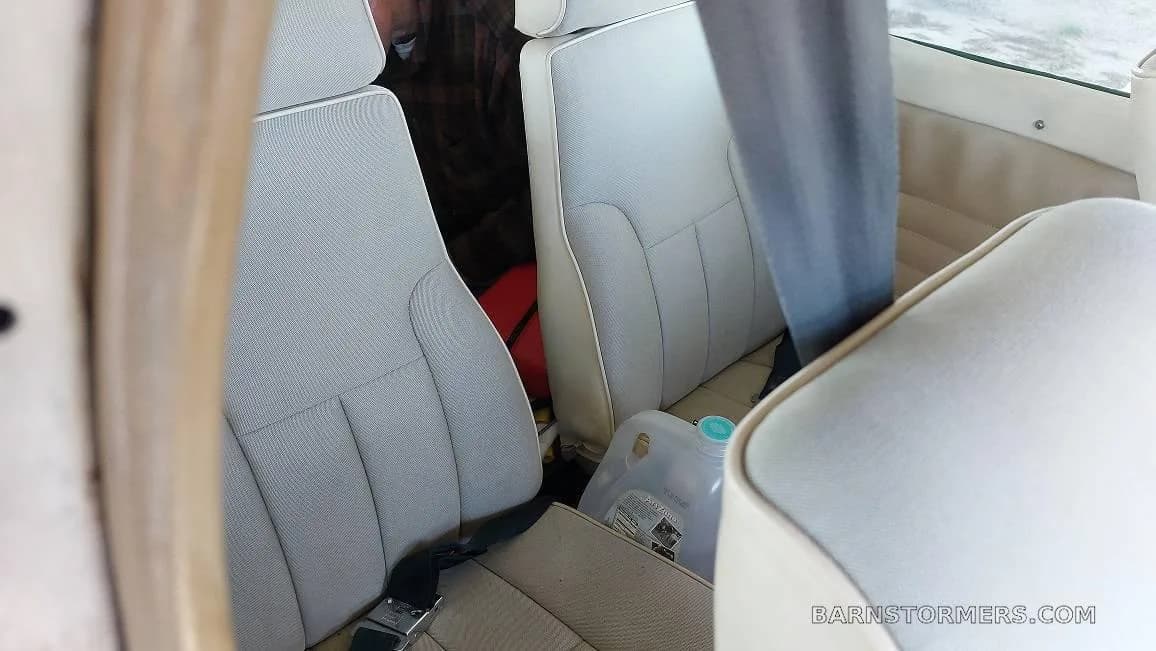 The light-colored passenger seats in the cabin of a small aircraft, with a water jug on the floor.