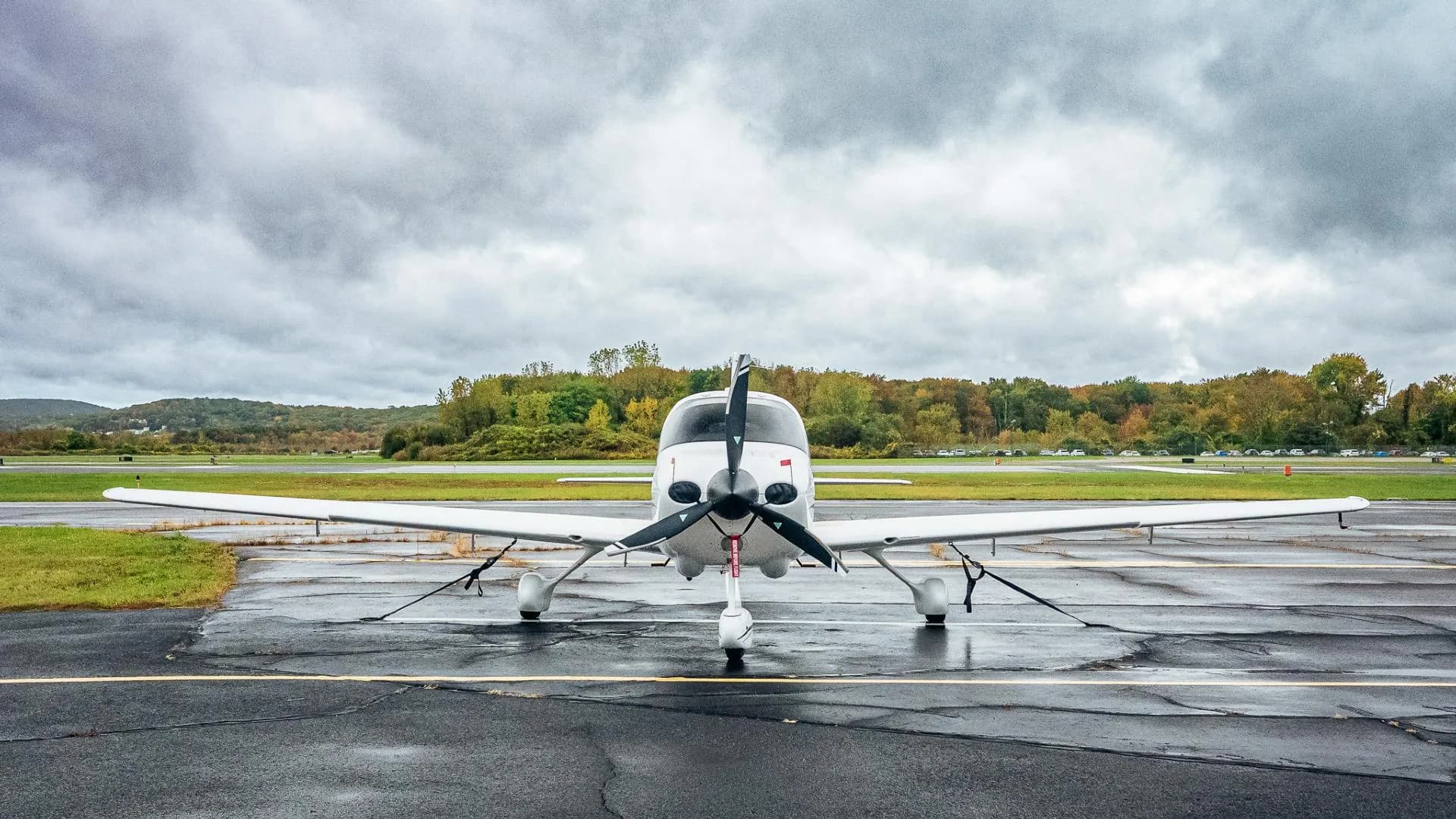 A head-on view of a white Cirrus SR20 aircraft with registration N899WT, parked on a wet tarmac under a cloudy sky.