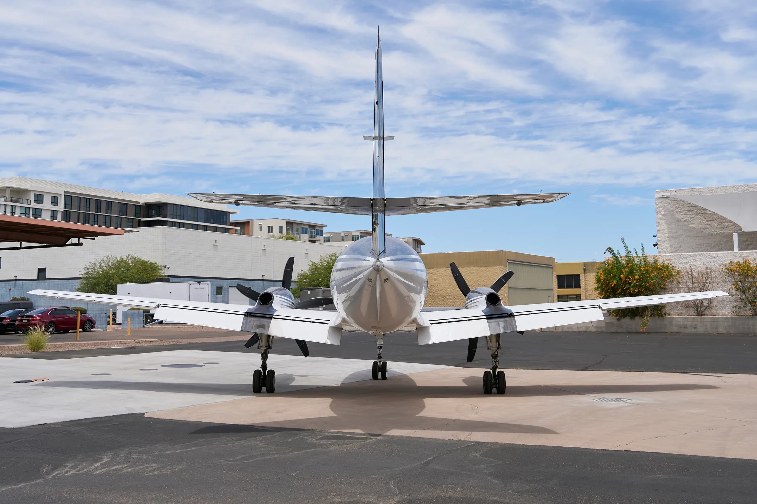 A rear view of the white and black twin-engine turboprop aircraft, N227JT, parked on a tarmac with buildings in the background.