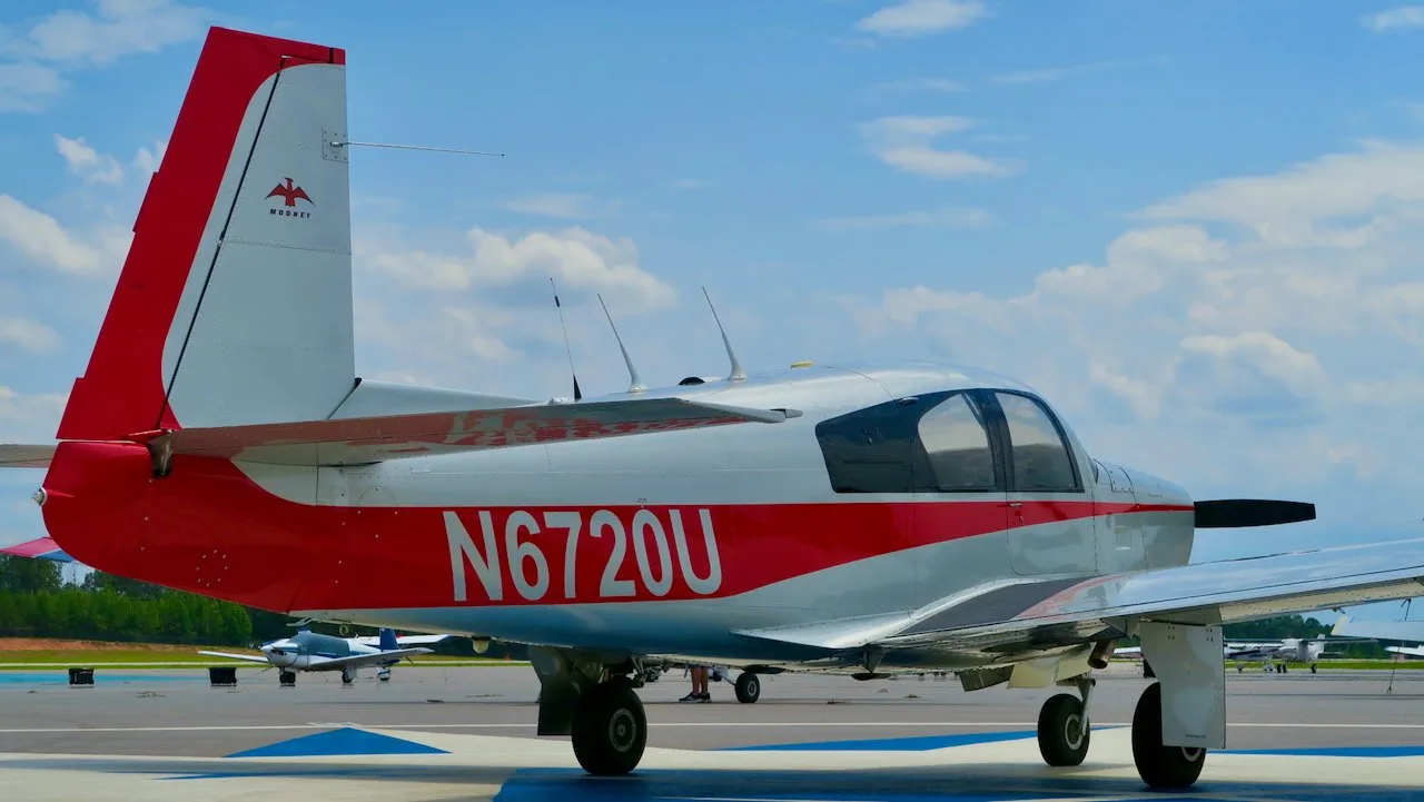 Rear-left view of a silver and red Mooney aircraft with registration N6720U on an airfield.