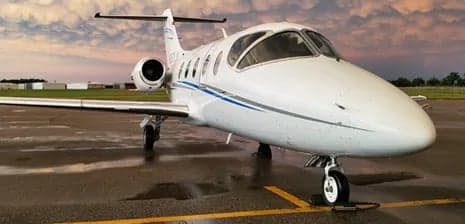 Front view of a white jet aircraft on the tarmac with a dramatic sky in the background.