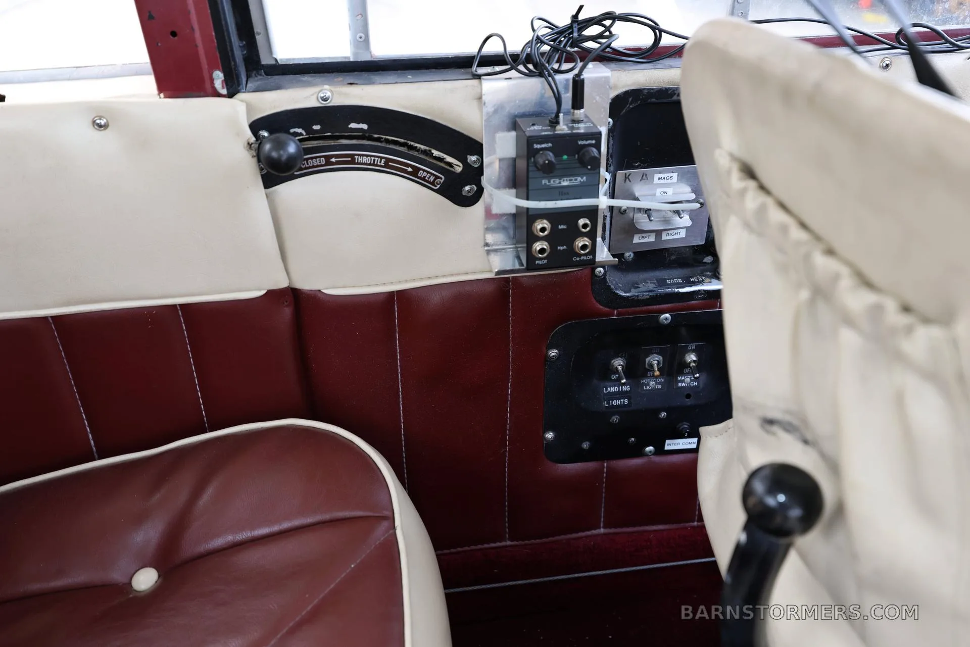 The interior side panel of the aircraft cabin, featuring a throttle control, audio panel, light switches, and red and cream upholstered seating.