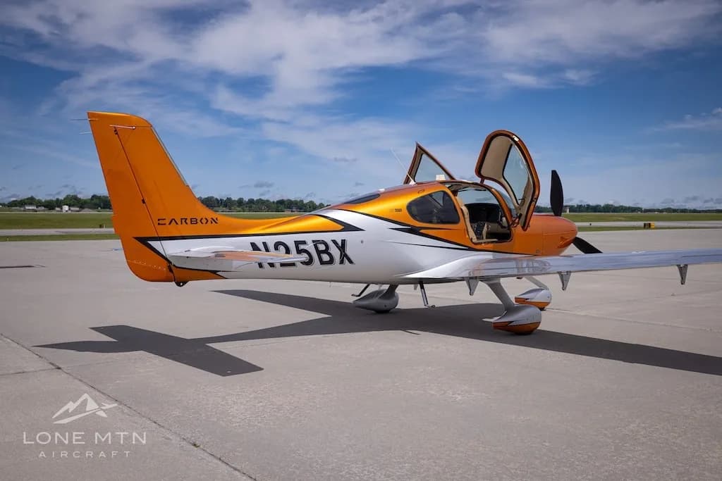 A side-left view of the orange and silver Cirrus SR22T N25BX with its doors open on an airfield.