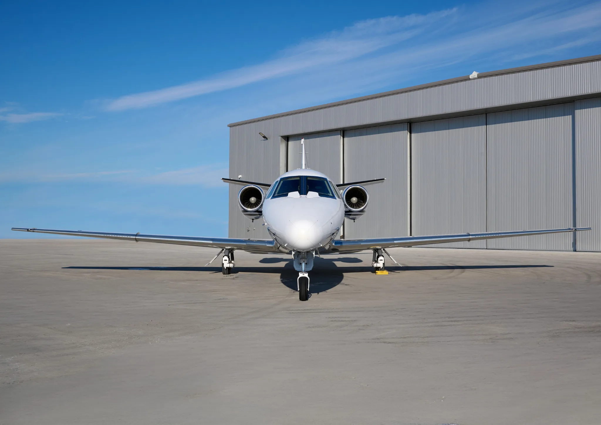 Front view of a white Cessna Citation CJ3 in front of a hangar.