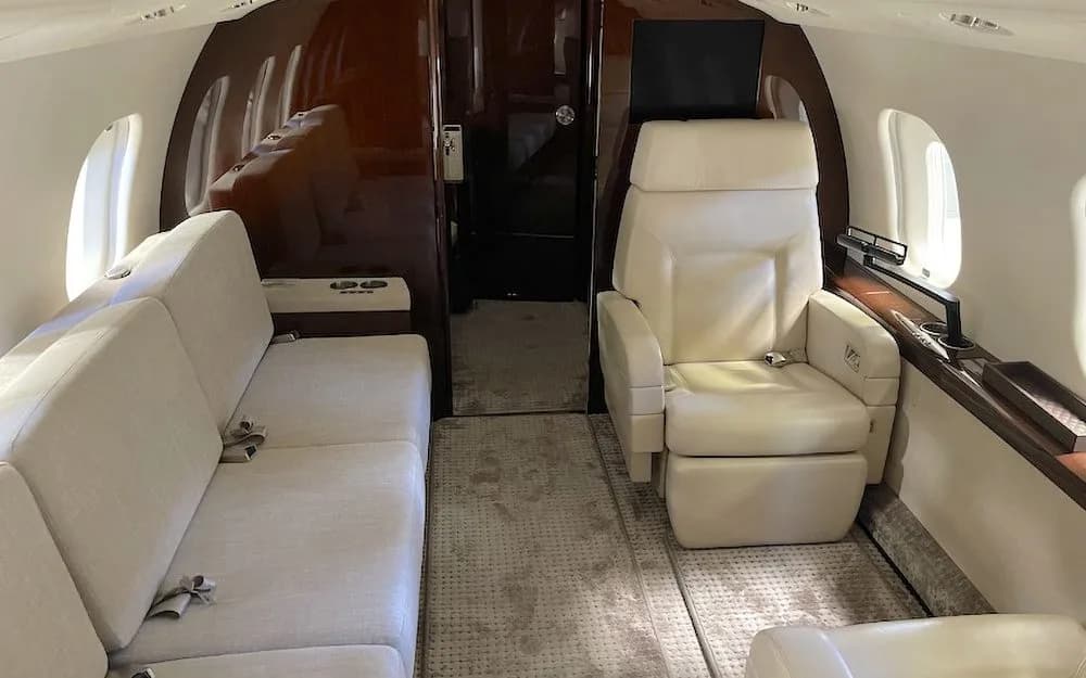 A private jet cabin section with a cream-colored sofa on one side and a single reclining seat on the other.