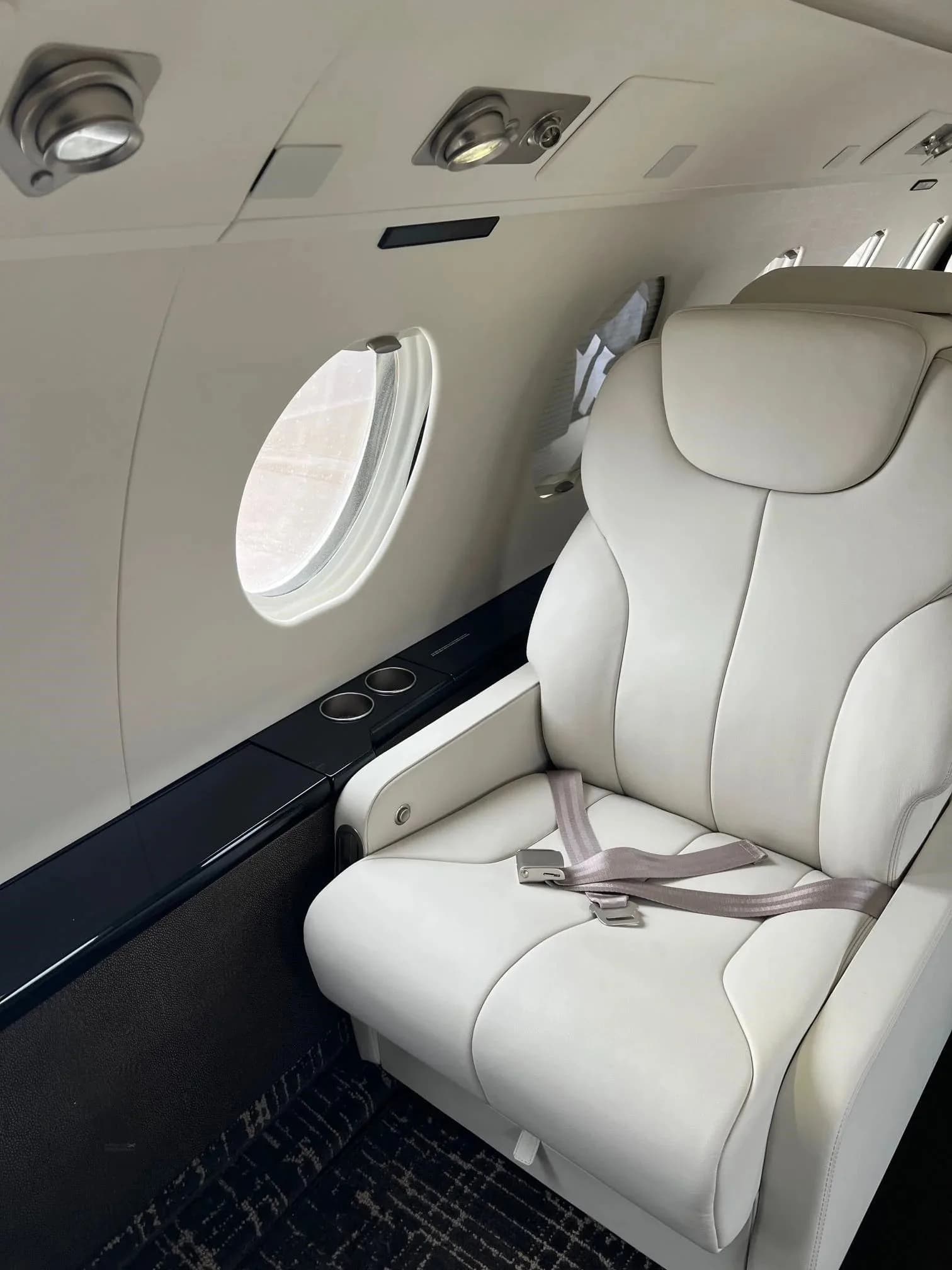 A close-up view of a white leather cabin seat next to a window in a business jet interior.