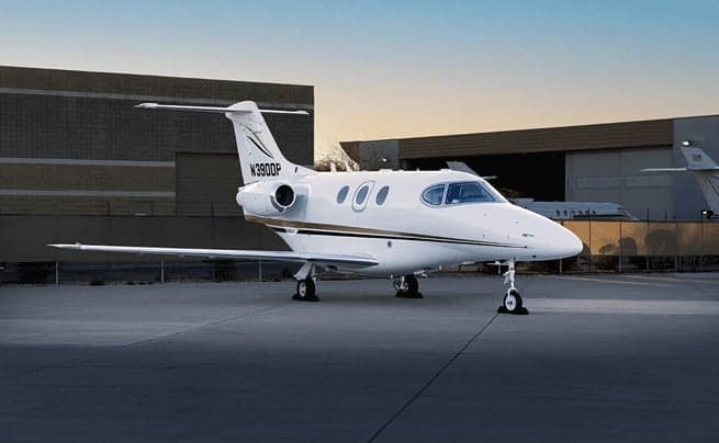 A white business jet with gold and black stripes, tail number N390DP, parked on an airport tarmac at sunset.