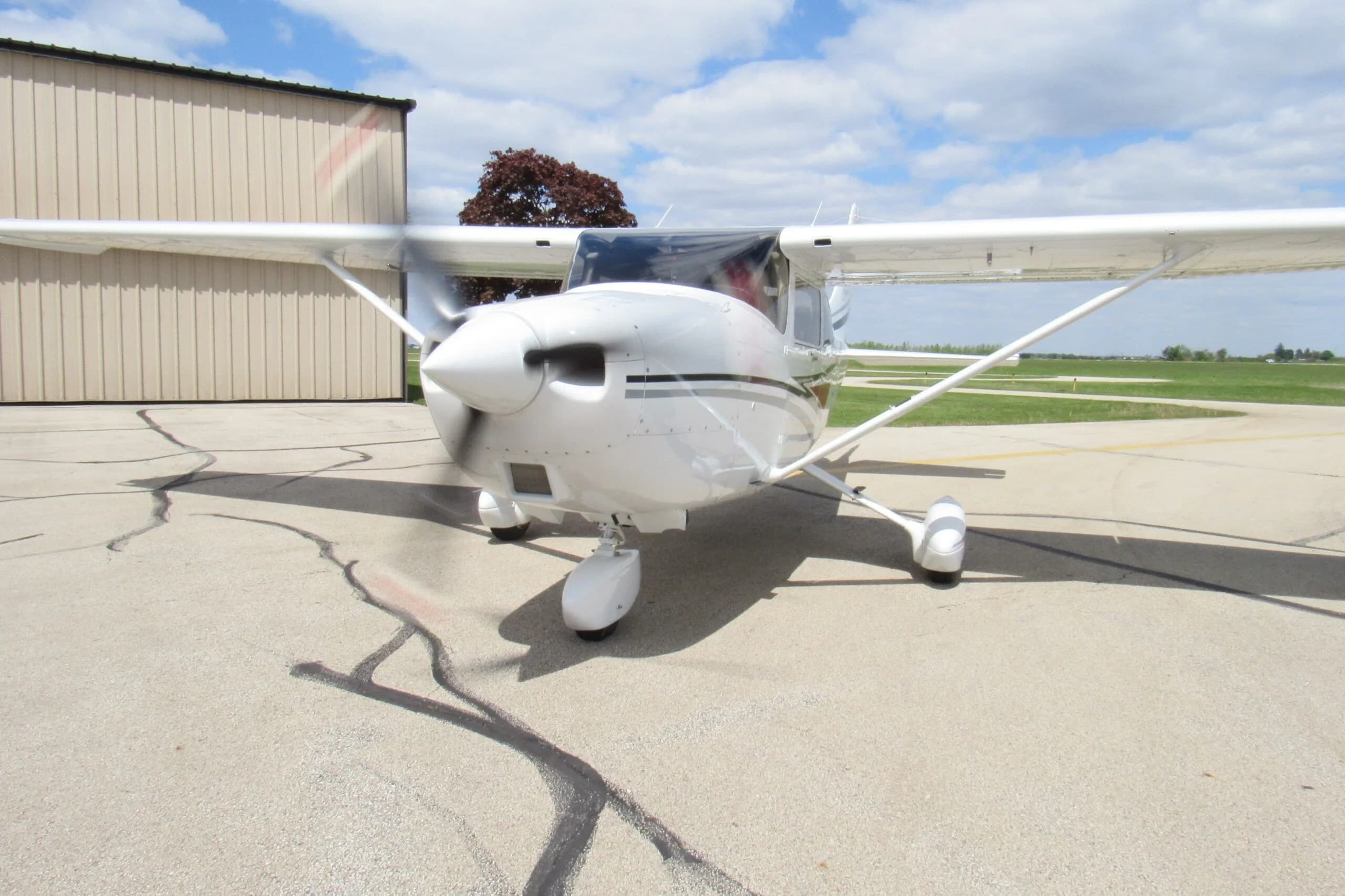 A front-right view of a white single-engine propeller aircraft with its propeller spinning on an airport tarmac.