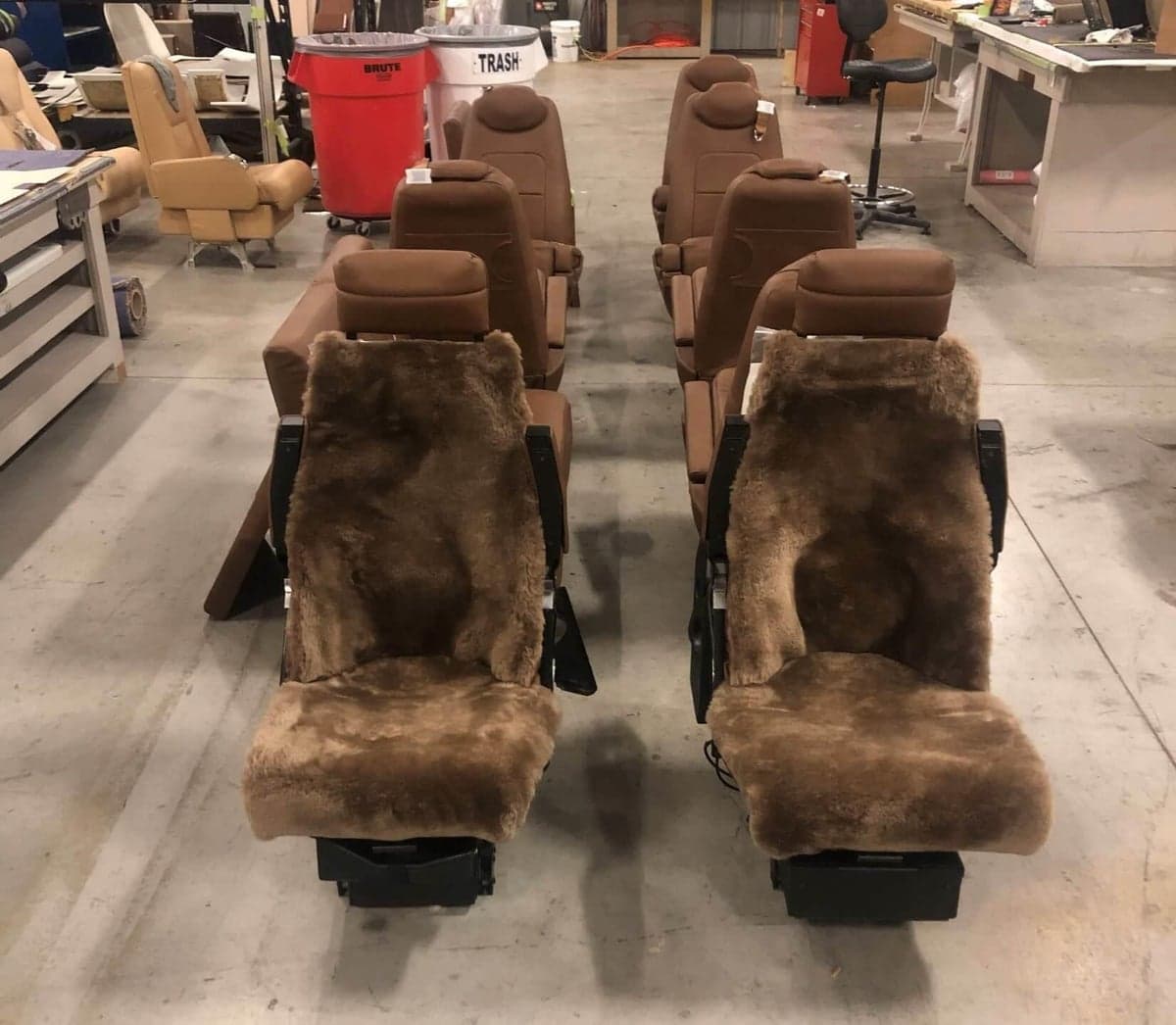 Aircraft seats with brown leather and sheepskin covers in a workshop setting.