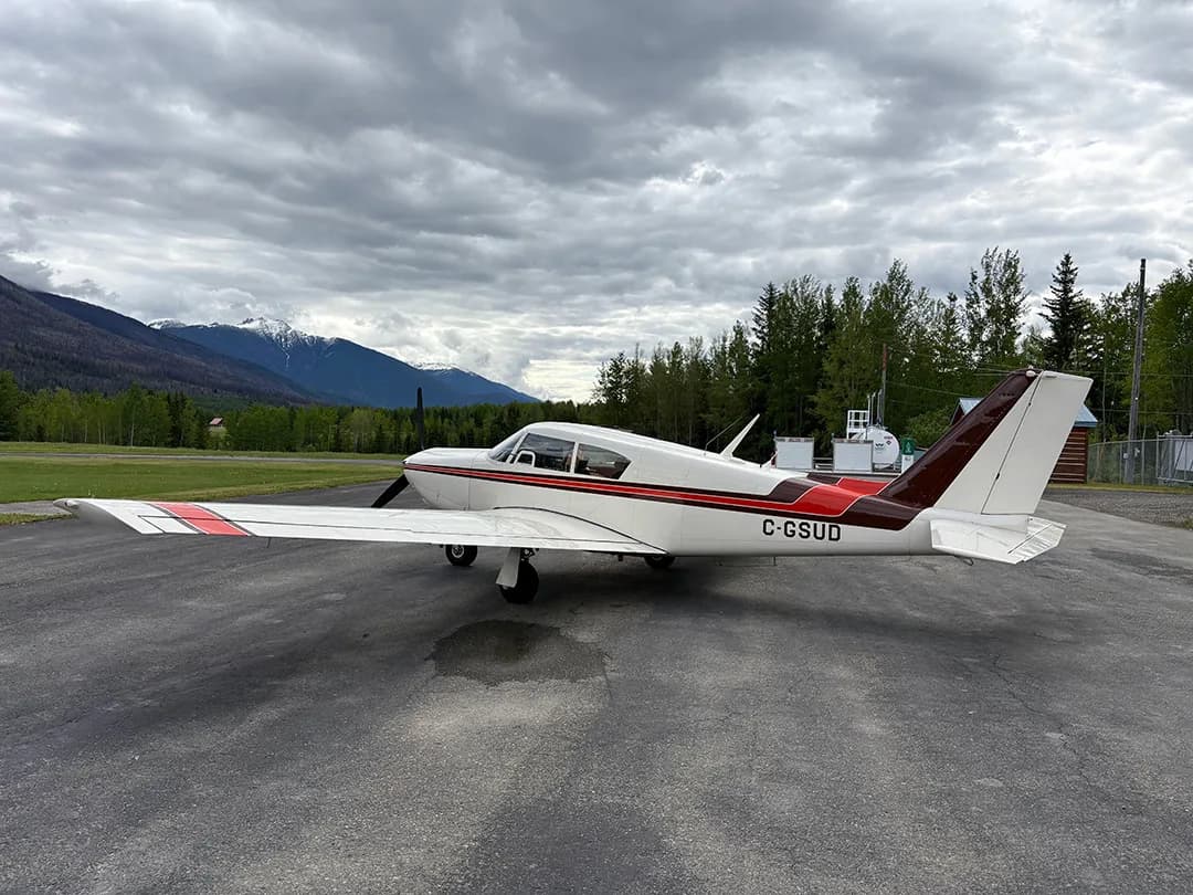 Side view of a white and brown aircraft with the registration C-GSUD parked on an airport tarmac with mountains in the background.