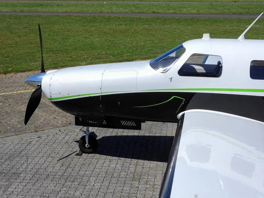 A close-up view of the propeller, nose, and front wing section of a white and black aircraft with green trim.