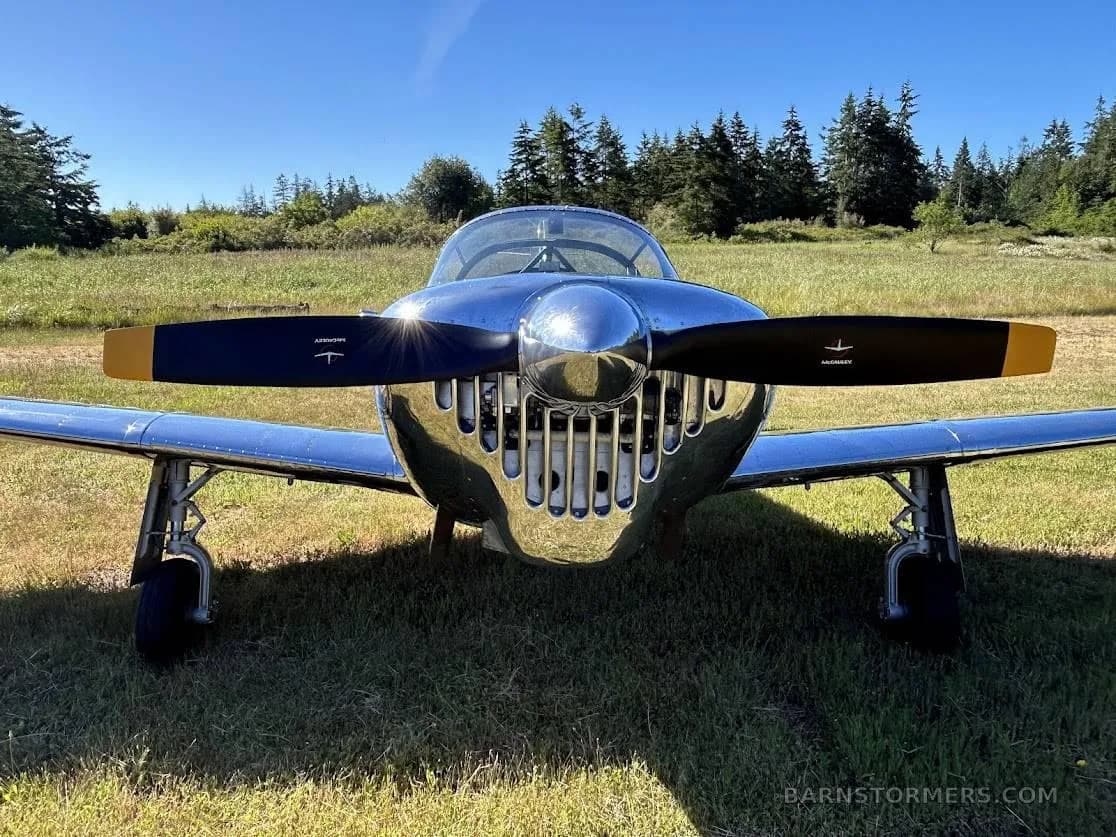 A head-on view of the polished silver aircraft, showing its propeller with yellow tips and the unique nose grille.