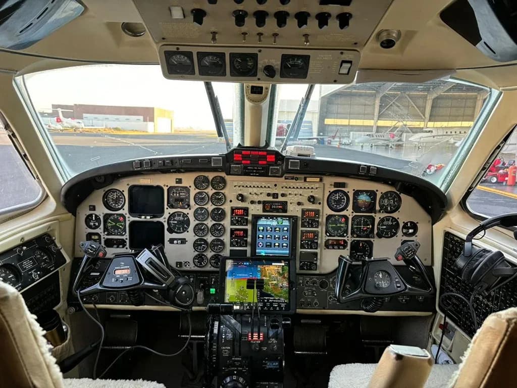 The detailed instrument panel and controls of a turboprop aircraft cockpit, with hangars visible through the windshield.