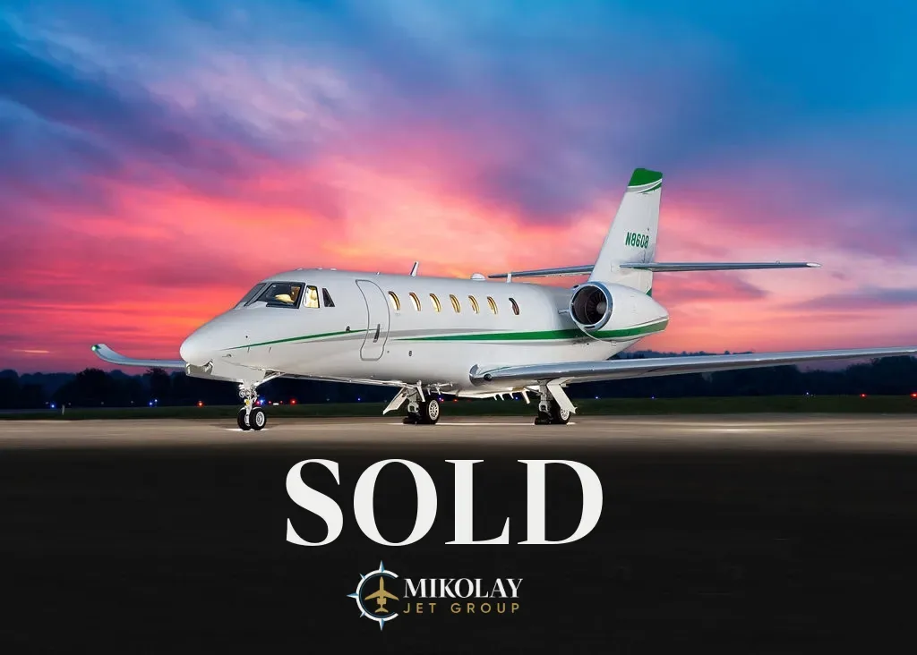 A white Cessna Citation Sovereign+ business jet with green accents on the tail and fuselage, parked on a tarmac at sunset, with "SOLD" text overlaid.