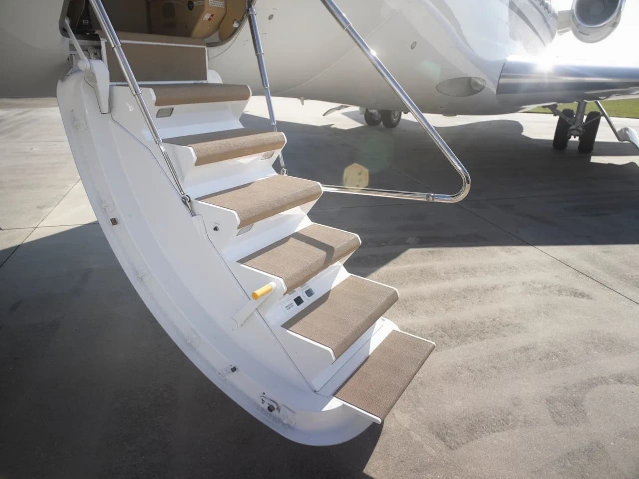 The extended airstairs of a private jet, with tan carpeted steps, leading up to the aircraft door.