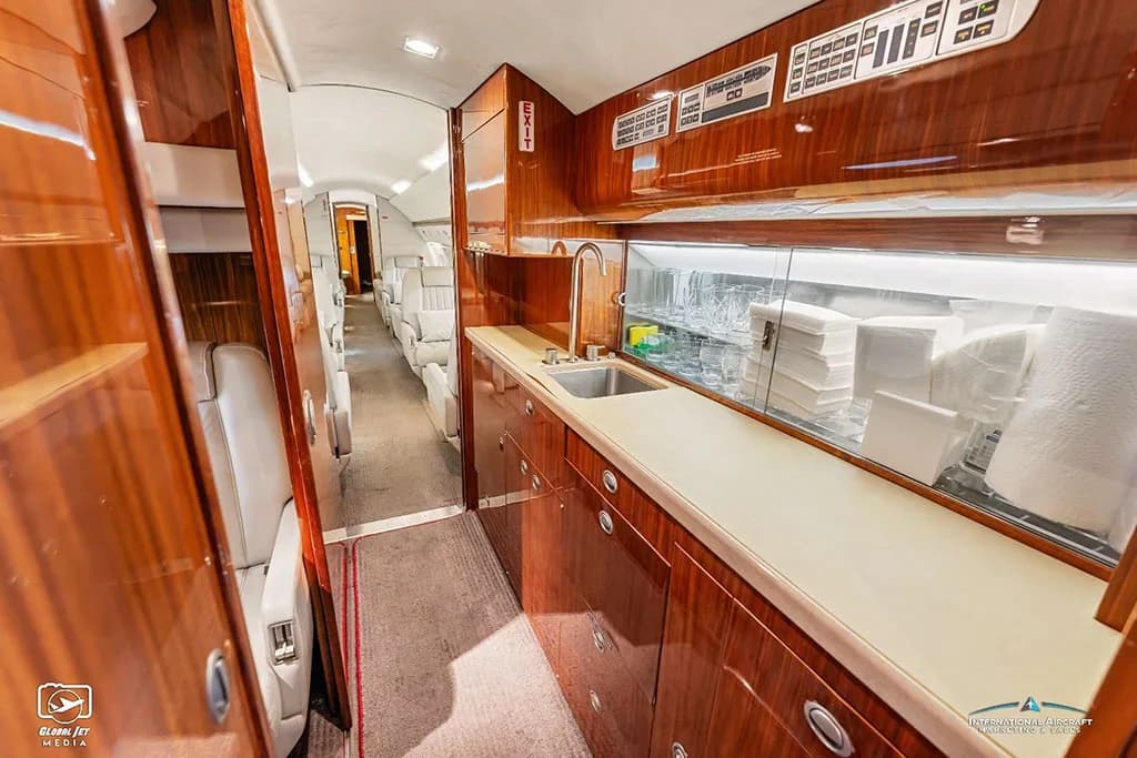The aircraft galley with polished wood cabinetry, a sink, and storage for glassware and supplies.