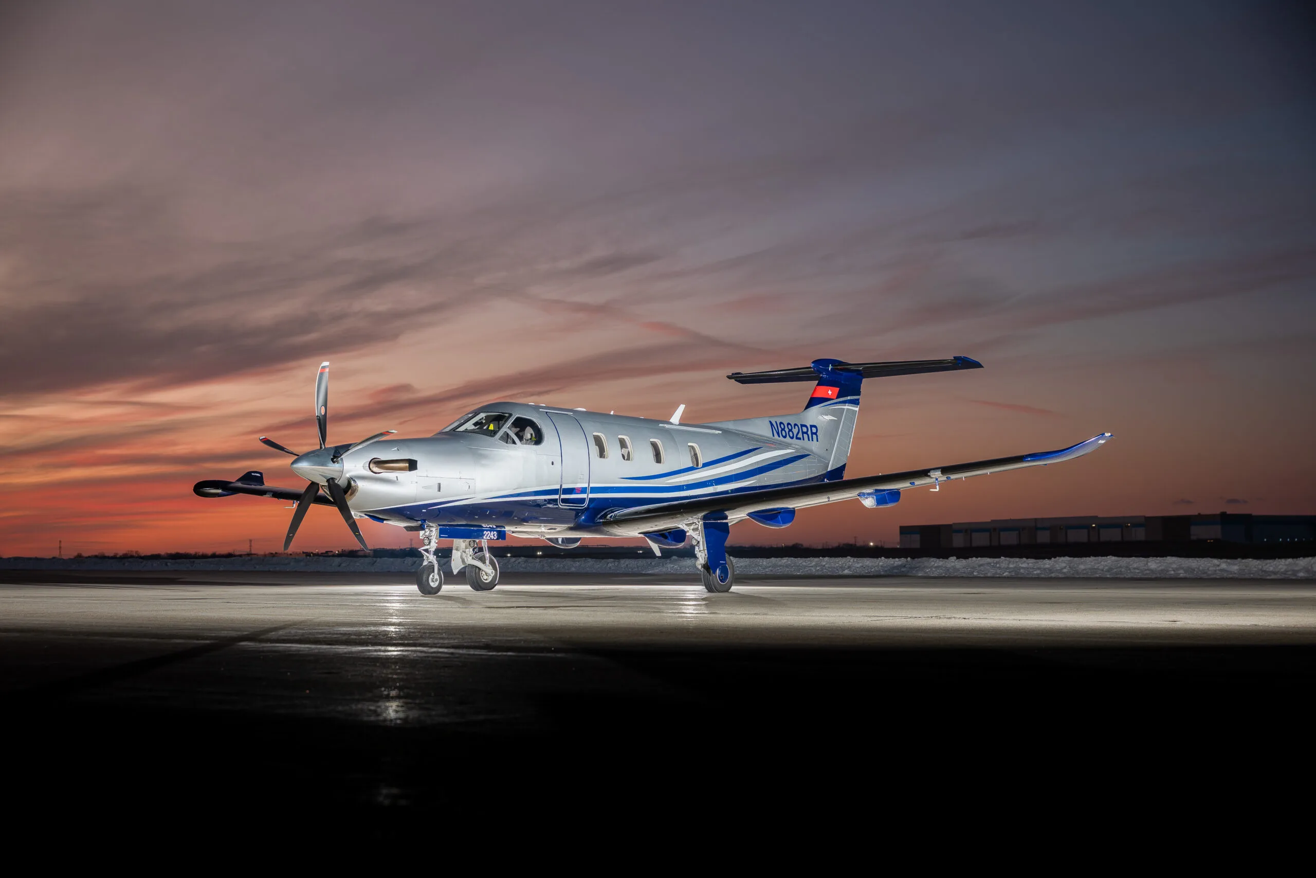 A silver and blue Pilatus PC-12 turboprop aircraft with registration N882RR is parked on a tarmac at sunset.
