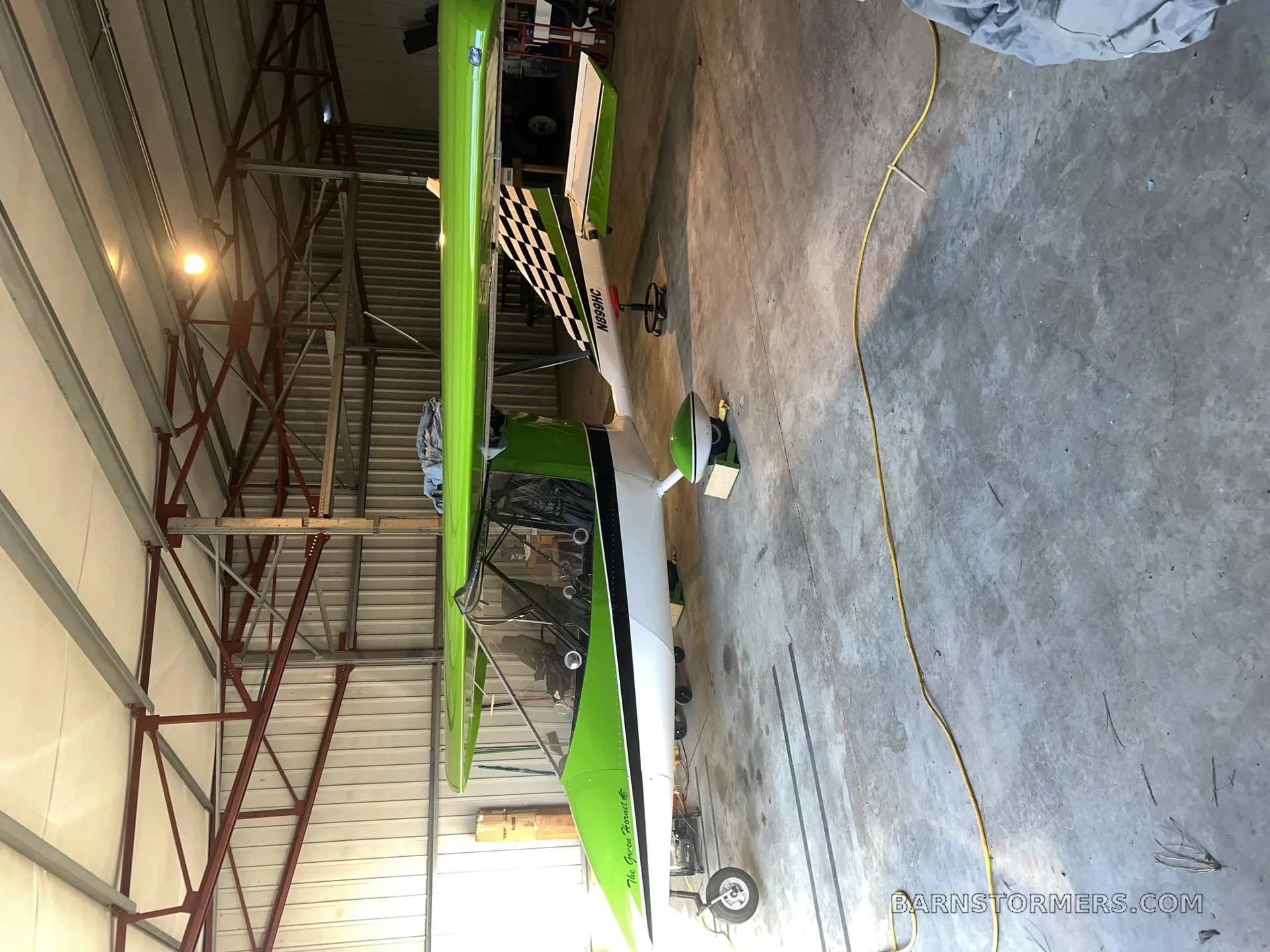 A bright green and white ultralight aircraft with a checkered tail is parked sideways inside a hangar.