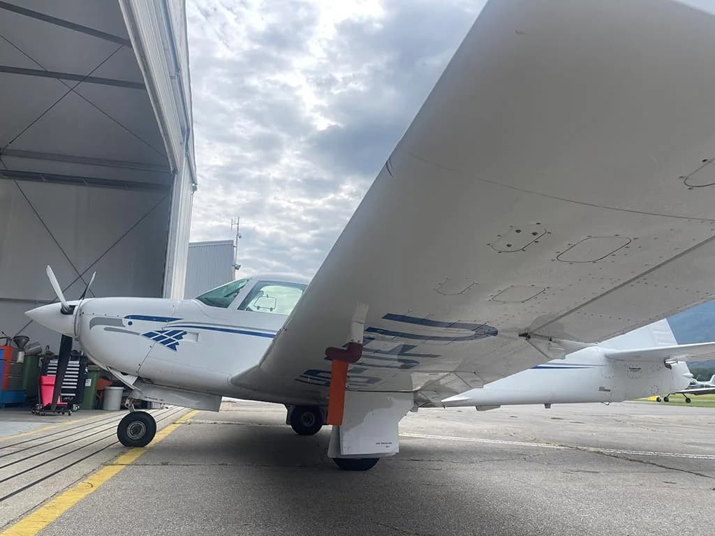 Underside view of the wing of a white single-engine propeller aircraft, parked near a hangar.